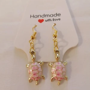 Handgjorda örhängen med rosa sköldpaddor - Söta handgjorda örhängen i form av sköldpaddor med guldiga detaljer och rosa mönster. Perfekta för att ge en lekfull touch till din stil.