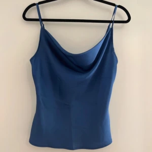 Blå linnetopp med draperad urringning - Säljer en stilren blå linnetopp med smala axelband och draperad urringning. Perfekt att matcha med jeans eller kjol för en snygg look.