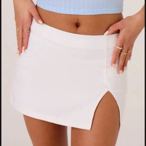 Vit kortkjol med slits - Säljer en stilren vit kortkjol med en snygg slits framtill. Kjolen har en enkel och modern design som passar perfekt till många olika outfits. Materialet känns mjukt och följsamt mot kroppen.