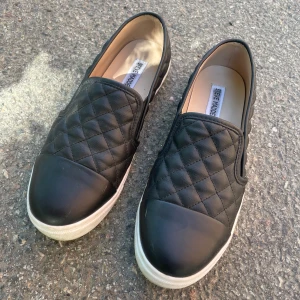 Steve Madden slip on skor - Steve Madden Zaander quilted slip-on. Knappt använda så i väldigt fint skick, har endast lite repor som syns på sista bilden. Storlek 9,5 motsvarar ca storlek 39. 💕