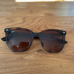 Ray-Ban  solglasögon - Klassiska Ray-Ban  solglasögon med bruntonade glas och mörkbrunt, nästan svart, plastbåge. Modellen är RB 4379D och har en design med silverdetaljer vid fronten. Perfekt accessoar för soliga dagar. Fordran tillkommmer