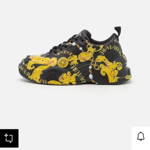 Versace Jeans Couture sneakers  - Säljer ett par svarta sneakers från Versace Jeans Couture med gult/guldigt mönster och logga. Skorna har snörning och rund tå. Perfekta för dig som vill sticka ut med en lyxig och unik stil. Har lite skavanker men bra skick, tyvärr finns inte kartong eller påse kvar då dom blev kvar hos mitt ex men digitalt kvitto finns! Inköptes för 2800kr men inte använt dom jättemycket. Står bara och dammar just nu så vill bli av med dom då jag kopplar dessa skor till mitt ex!