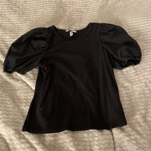 Svart topp med puffärmar - Säljer en svart topp med rund halsringning och stora puffärmar. Perfekt för att ge outfiten lite extra volym och stil!! Från H&M i storlek S💕 