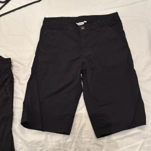 Svarta shorts från KappAhl - Svarta shorts från KappAhl med klassisk design och normal passform. Shortsen har snedställda fickor fram, en bakficka med dragkedja och stängs med knapp och dragkedja. Perfekta för sommardagar.