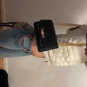 Svart axelväska med guldkedja - Säljer en svart axelväska från Michael kors i croco-mönstrat syntetmaterial. Väskan har guldfärgade detaljer, kedjerem och ett dekorativt spänne framtill. Perfekt för dig som vill ha en trendig accessoar med lyxig känsla. Original pris 4700 men kan tänka mig sälja för 2500 men priset kan diskuteras, original förpackning finns 