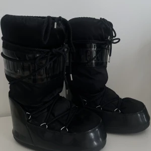 MOONBOOT W GLANCE - Svarta Moon boots med blancka svarta detaljer! Skorna är super sköna när det är snö och lätta. Har använt dom mycket så dom är formade efter foten på insidan. Men utsidan ser dom som nya ut.💗
