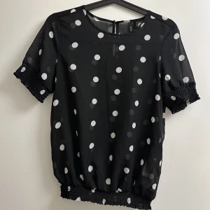 Prickig t-shirt - Svart t-shirt med vita prickar i ett halvt genomskinligt material. Resår i nederkant och ärmar. 