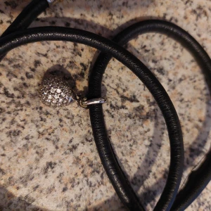 Läderarmband med silver/swarowski berlock - Droppe i silver med swarowski på svart lädersnodd som viras flera varv med magnetlås. 71 cm