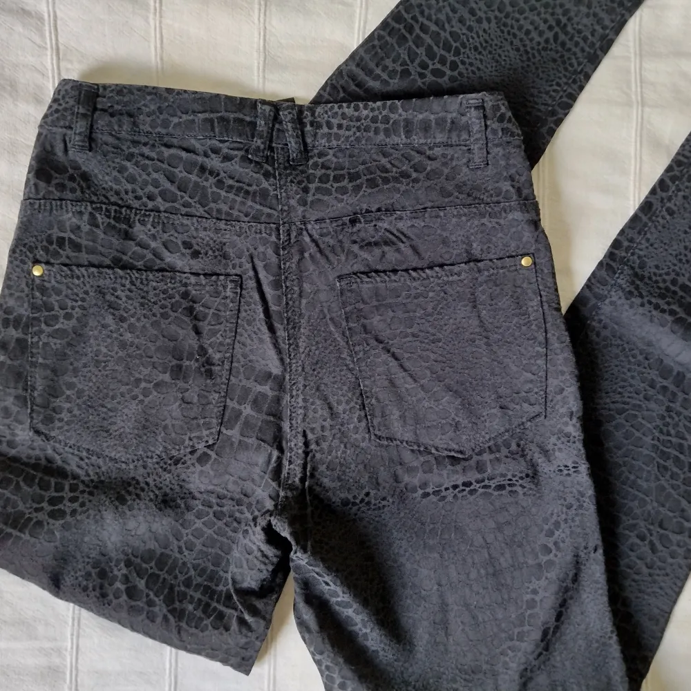 Snygga svarta/mörkgrå högmidjade byxor med guldfärgade detaljer från H&M. Sytt snakeskininspirerat mönster. Tyget är pyttelite nopprigt/ludet på vissa ställen. 55% viskos 41% bomull 4% elastan. Storlek 36. . Jeans & Byxor.