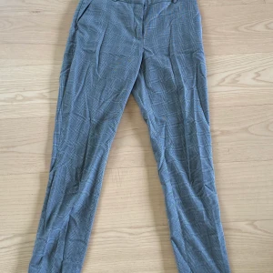 Rutiga kostymbyxor  - Gråa rutiga kostymbyxor med en tightare fit. Storlek 36 och därmed små för min som vanligtvis har 38/40. Fina både till vardags och festligare tillfällen! Har ett mindre hål precis under rumpan som syns på bild 2, inget som jag märkt av!