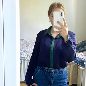 Blå skjorta med gröna detaljer - En blå polyesterskjorta med grön krage och gröna detaljer på ärmarna. Den har två bröstfickor. 