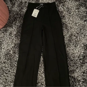 Svarta raka Pull&Bear byxor - Svarta byxor i storlek XS. Köpta för 300 kr men säljs nu för 200! Dem är inte använda alls, dem är ganska långa med raka ben, sitter mycket fint i midjan