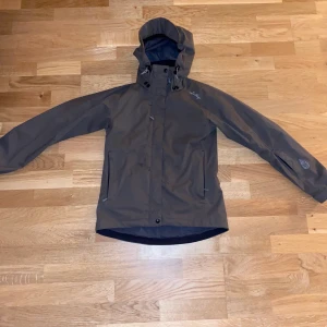 Lundhags Skaljacka  - Brun Skaljacka från Lundhags.  Otroligt sparsamt använd, mycket fint skick.   2-lager. Vatten & vindtät.  Strl.34