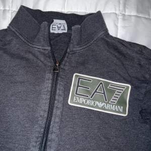 En fin mörkgrå Armani (ea7) tröja med zipper. Märket är i reflex och är delförklaring svår att få en bra bild på tröjan i helhet. Men de är mörkgrön färg i märket också. Storlek M