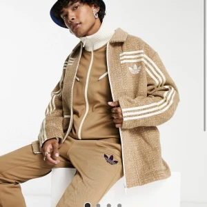 Adidas  - Säljer denna brun jacka i 70-talsstil med krage från Adidas Originals. Jackan är ny! Nypris: 1759kr(asos) 