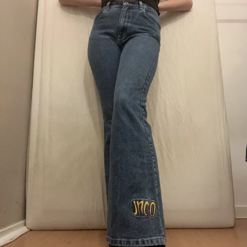 Blå jeans med gul detalj nertill på vänster ben från JNCO. Fint skick. Midmidjade och utsvängda. obs: ungefärliga mått: Midjemått: 78cm. Innerbenslängd: 82cm. . Jeans & Byxor.
