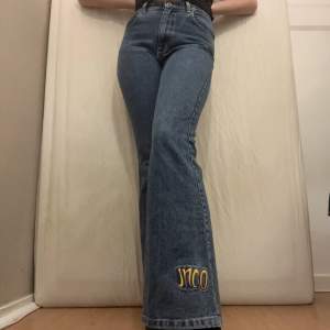 Blå jeans med gul detalj nertill på vänster ben från JNCO. Fint skick. Midmidjade och utsvängda. obs: ungefärliga mått: Midjemått: 78cm. Innerbenslängd: 82cm. 
