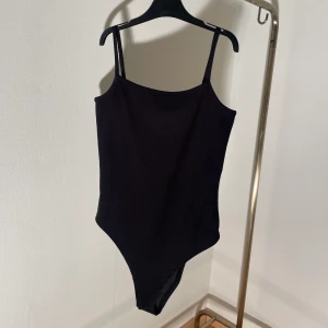 Body - Svart body, ribbad i tyget (se sista bilden). Den knäpps undertill med knappar. Använd 1-2 gånger så nyskick. 