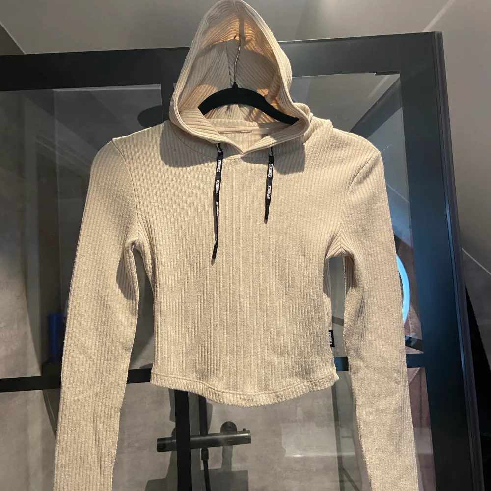 Beige ribbad tröja ifrån stronger. Croppad tight långärmad med luva och band. Tröja är i strl Xs och i bra skick. Bud om fler är intresserade❤️. Hoodies.