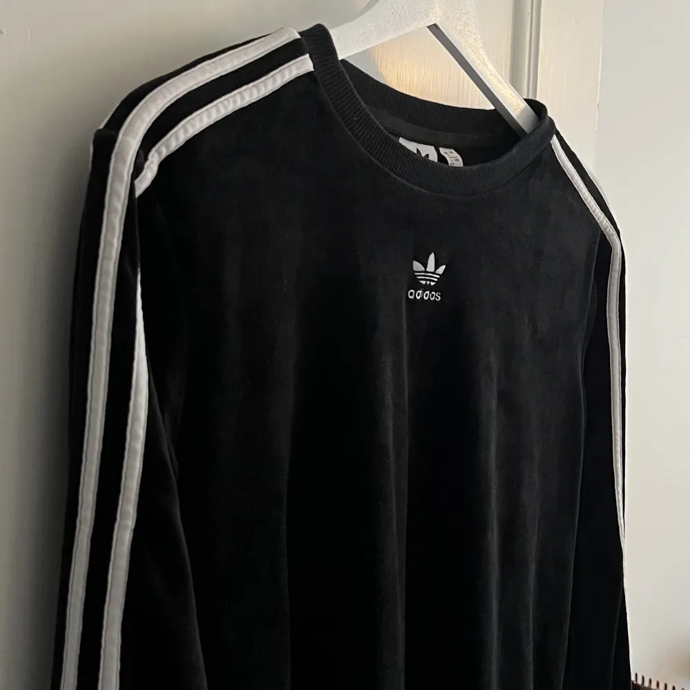 En otroligt fin retro adidas -tröja i svart med ränder på ärmarna och loggan i mitten på bröstet. Detta är det lenaste plagget jag äger, materialet är som velvet 💘 Bara använd ett fåtal gånger så otroligt bra skick!. Toppar.