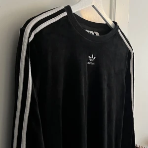 Retro Adidas velvet sweatshirt - En otroligt fin retro adidas -tröja i svart med ränder på ärmarna och loggan i mitten på bröstet. Detta är det lenaste plagget jag äger, materialet är som velvet 💘 Bara använd ett fåtal gånger så otroligt bra skick!