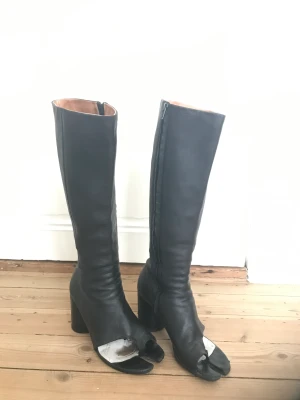 Maison Margiela tabi boots stl 40 - Nypris ca 15000. Klassiskt modeobjekt i lyxig kvalitetsläder från det legendariska modehuset Maison Martin Margiela i Paris.  Knähöga stövlar/boots i mjukt lammskinn med sidenmatt lyster.  Öppen tå i klassisk Tabi-design. Sula i kalvläder. Bra skick.