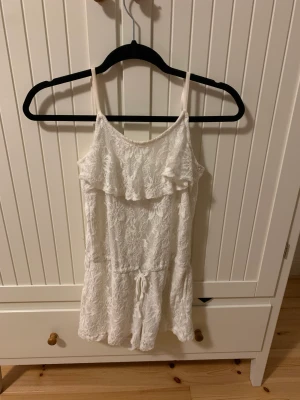 Jumpsuit - Vit jumpsuit. Övre lagret är spets. Under spetsen är det ett vitt tyg. Den är inte genomskinlig. Storlek 146/152