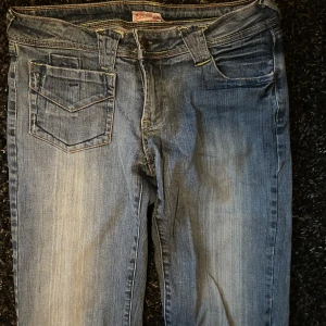 Y2K lågmidjade jeans strl 34 - Lågmidjade jeans köpta under tidigt 2000-tal i storlek 34. Knappt använda med knappar på bakfickorna och raka ben