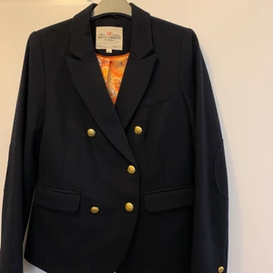 Så snygg kavaj fr Holly and Whyte strl m - I fin ull och med vackert innerfoder. Färg mörkblå.  Figursydd kort modell med fina detaljer som guld knappar. I perfekt skick! Bara använd några få ggr. Har hängt bredvid luddig kofta som luddat av men kommer rollas fin innan försäljning.