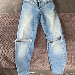 Blåa skinny jeans med hål - Blå skinny jeans med hål på som är använda mycket men inte som man kan se så förutom att de är lite urtvättade. Från never denim i strl xs som passar bra i längden på mig som är 166 cm men försmå i midjan på mig därför säljer jag dessa nu.