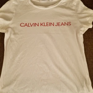 2 st Calvin Klein t-shirtar - Säljer 2 st vita t-shirts av märket Calvin Klein.  1. Köpt på Kids Brand Store, bra skick utan märken, storlek 164/176. Vit med svart CK tryck. 2. Köpt på Johnells, bra skick utan märken, storlek S (dam), vit med röd tryck.  Säljs endast tillsammans. 