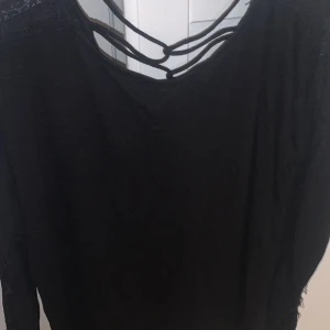 Svart tröja - Svart tröja, ”spets” på armarna och lite öppen nacke/rygg med snör mönster. 