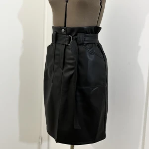 Midikjol med skärp i skinnimmitation - RW coated kjol med mjuk linning och hög midja.  Ingår midjebälte.  Lite stretch i materialet.  Fint skick, använt fåtal gånger. Rekommenderar att hänga/vika varsamt för att slippa hålla på med veck!   Storlek   med b: 