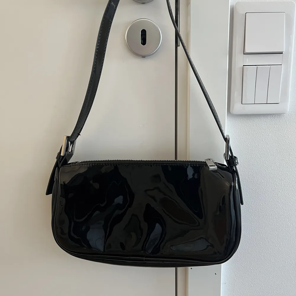 En svart väska i fint skick från Gina Tricot. Den är i lackliknande material på utsidan. Finns inga fläckar eller liknande på insidan . Accessoarer.