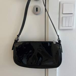 En svart väska i fint skick från Gina Tricot. Den är i lackliknande material på utsidan. Finns inga fläckar eller liknande på insidan 