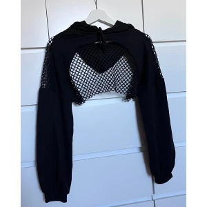 Croppad Hoodie - En kort huvtröja med nä på rygg och armar. Köpt för 2-3 år sedan men endast använd en gång. Storlek M men passar de flesta eftersom den endast sitter fast över armarna 