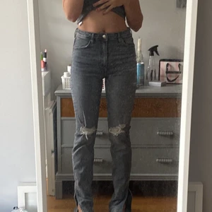 Gråa högmidjade jeans - Fina gråa jeans från Zara. Hål på knäna och slits. Säljer för att de tyvärr inte kommer till användning längre då det har blivit för korta och inte längre är min stil. Priset kan diskuteras.