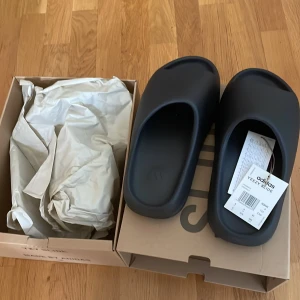Adidas YEEZY slides Onyx/svarta - Skorna är i nyskick och helt oanvända. Lådan har inga skador och följer såklart med i köpet. 