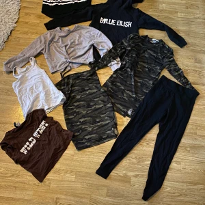 Klädpaket storlek 140 - Kläder till tjej i storlek 140, alltihop i fint skick! - Billie Eilish-tröja - 2 par svarta leggings - 2 camo-klänningar - 1 croppad ljus tröja - 2 croppade t-shirts  - 2 vita linnen - 1 vit topp  Finns på fler sidor