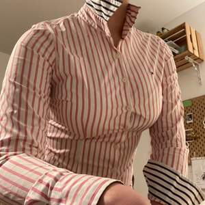 Äkta Tommy Hilfiger skjorta med fina reversibla detaljer, marinblå och rosa ränder. Jättefint skick, som ny. Storlek XS-S, säger stretch men jag tycker att den sitter tajt.