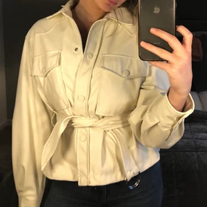 Vårjacka - Jacka från Bershka. Inga jättesynliga tecken på användning. Beige med knappar och snöre i midjan. Man kan använda utan snöret också som en vanlig jacka - vilket är superfint också! 
