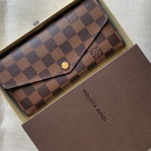 Louis Vuitton Sarah Plånbok (Nyskick) - Plånbok i brunt läder från Louis Vuitton, modell Sarah. Plånboken är mycket sparsamt använd och minimalt slitage syns enbart på guldknappen på plånbokens framsida.   Kvitto saknas då jag fått den som present för ett par år sedan, originalask medföljer.