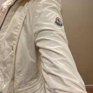 Moncler Vindjacka - Säljer denna fina monclerjacka som är i nyskick!🤩 Inköpt här på Plick av en tjej som köpt den på Vesteire Collective. Storlek 0, vilket motsvarar 34 (xs-s)🤍 Såklart äkta! Går att ta bort luvan med hjälp av en dragkedja. 