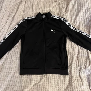 Puma tjocktröja med dragkedja  - Svart pumatröja med dragkedja, står puma på armarna och finns fickor med dragkedja 