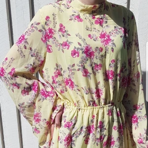 Blommig klänning från NA-KD strl 40 - Endast provad, stretch i midjan, långa trumpet ärmar, öppen rygg och långa knytband i nacken. Är gjort i tyg 100% polyester, storlek 40. Hel och fin.