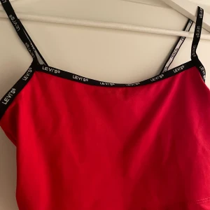 Levis top - Röd Levis topp med svarta smala band. Toppen slutar ovanför naveln under bysten, något kortare. Storlek xs