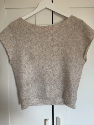 Beige stickad topp från Nelly - Mysig beige stickad topp från Nelly i storlek XXS. Toppen har en enkel, rak passform och är ärmlös. Perfekt att styla med jeans eller kjol för en avslappnad look.