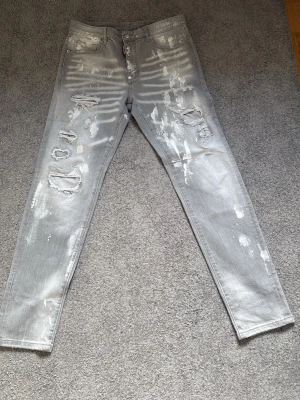 Dsquared jeans  - Säljer ett par grå jeans med distressed detaljer och stora hål på framsidan. Jeansen har en tvättad look med vita slitningar och raka ben. Klassisk femficksmodell och knappgylf. Perfekta för en edgy streetstyle.