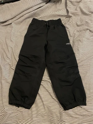 Svarta täckbyxor från Kayoba - Säljer ett par svarta täckbyxor från Kayoba Outdoor. Byxorna har resår i midjan och vid bensluten för extra komfort och passform. Perfekta för kalla dagar och utomhusaktiviteter. Materialet är slitstarkt och vattenavvisande.