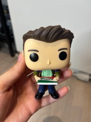 Joey Tribbiani Funko Pop figur Friends - Joey Tribbiani Funko Pop från serien Friends/Vänner. Figuren håller i en liten pizzakartong med texten 'Pizza' på locket. Perfekt för samlare eller som dekoration. Ny skick men ingen kartong. 